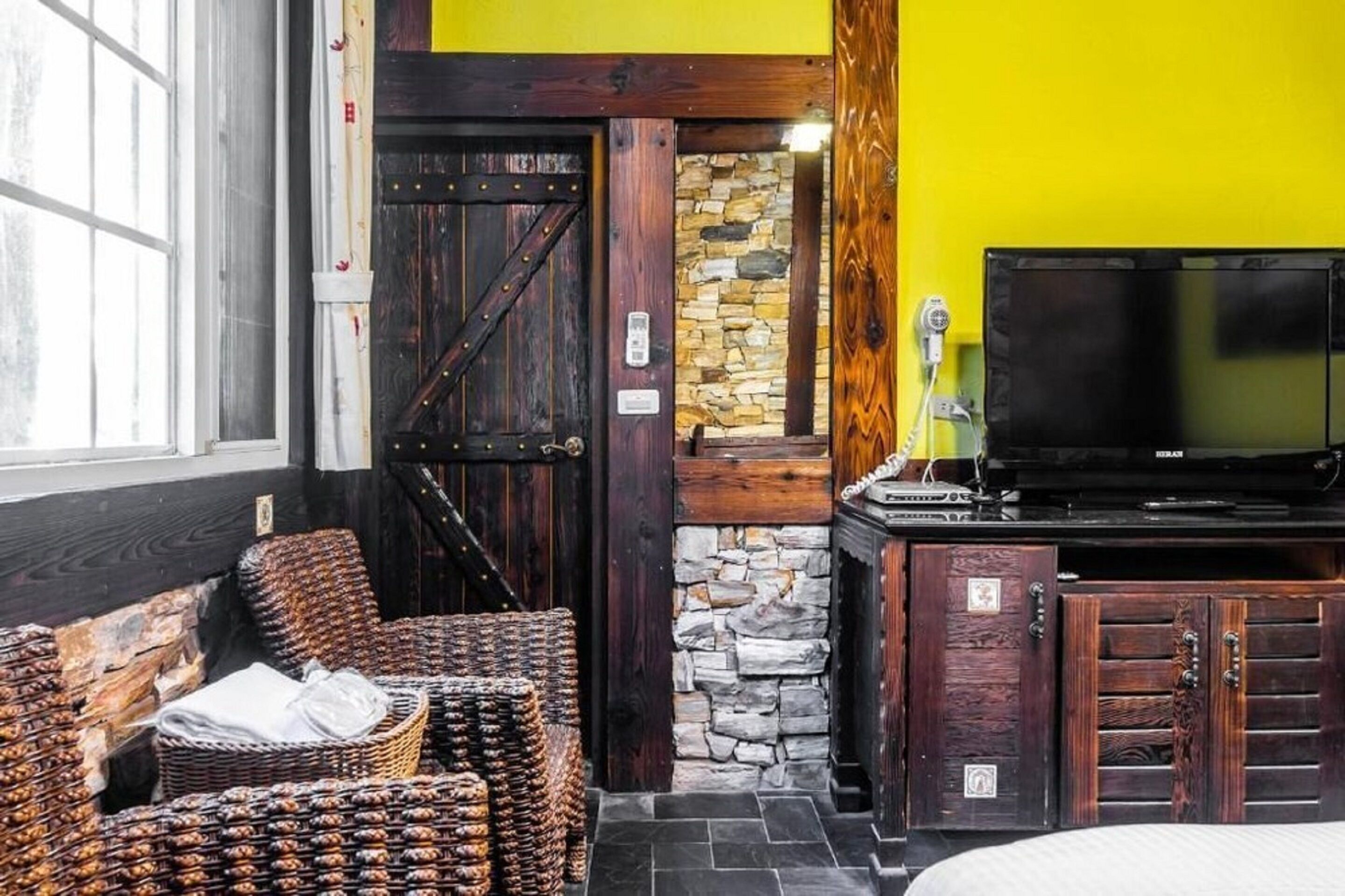 A room with wicker furniture, a stone wall, a wooden door, and a television.