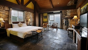 A room with a bed, two wicker chairs, a television, and stone walls. - Provence Rose Lodge in Ching Jing (Ren'ai)