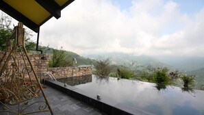 An infinity pool with a stone wall and metal sculpture, overlooking a mountainous landscape. - Provence Rose Lodge in Ching Jing (Ren'ai)