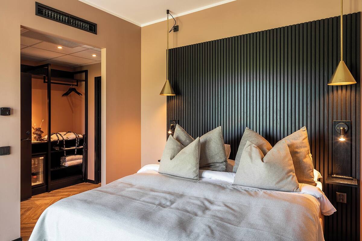 A modern hotel room with a large bed, a wardrobe, and a bathroom visible through an open door.