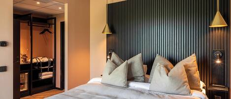 A modern hotel room with a large bed, a wardrobe, and a bathroom visible through an open door.