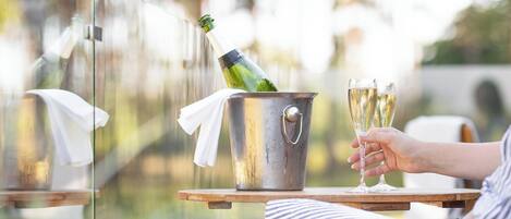 A person holding two champagne glasses, a bucket with a bottle, and a white cloth on a wooden table outdoors.