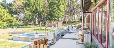 An outdoor deck with wooden furniture, a pool, and a view of a forest.