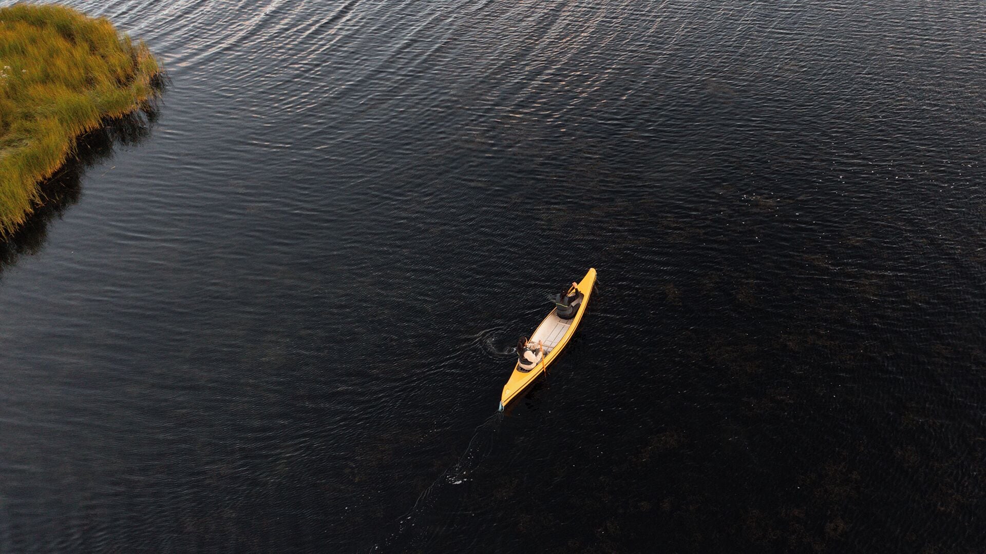 Una canoa sobre un cos d'aigua tranquil·la, amb una petita illa a l'esquerra.