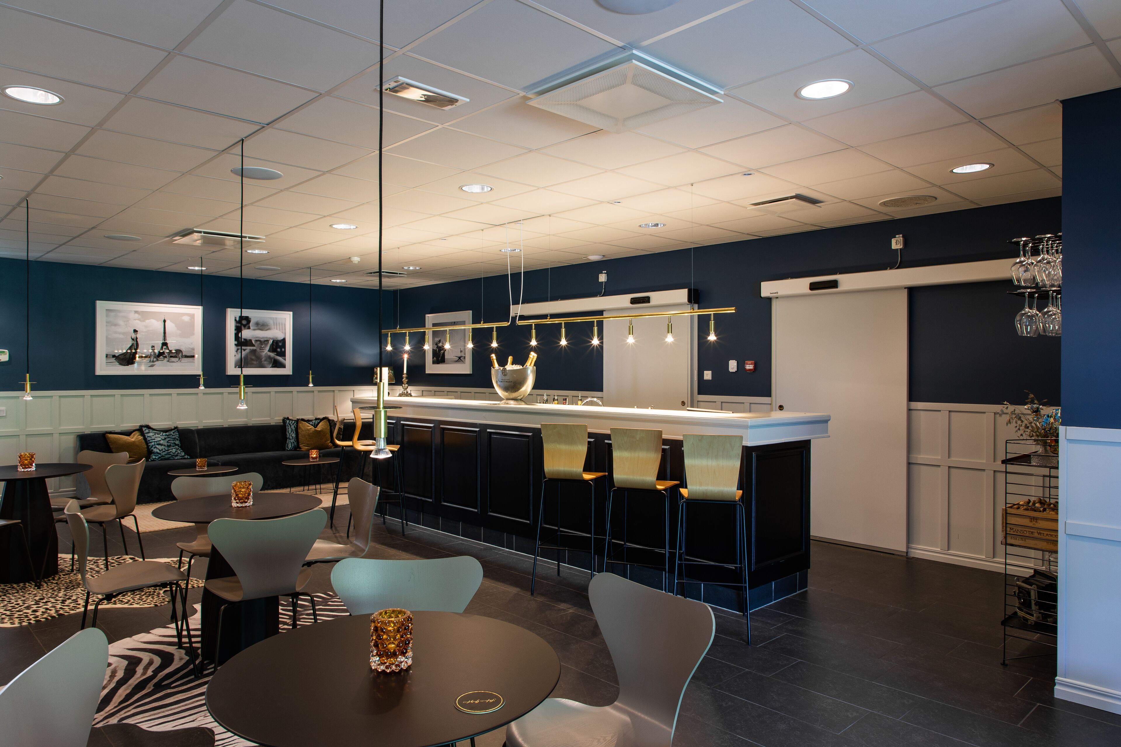 Un espace bar moderne doté d’un comptoir, de sièges et de luminaires suspendus.