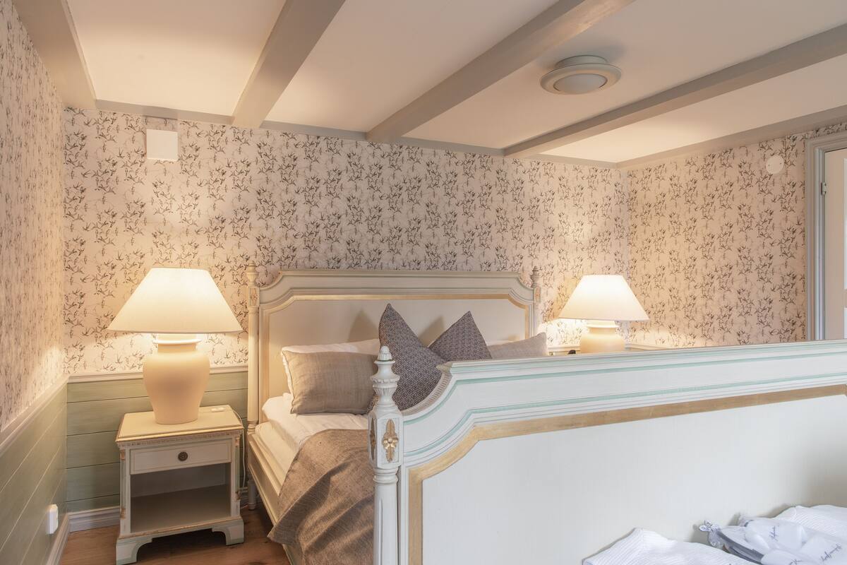 A bedroom with a bed, two bedside lamps, a nightstand, and floral wallpaper.