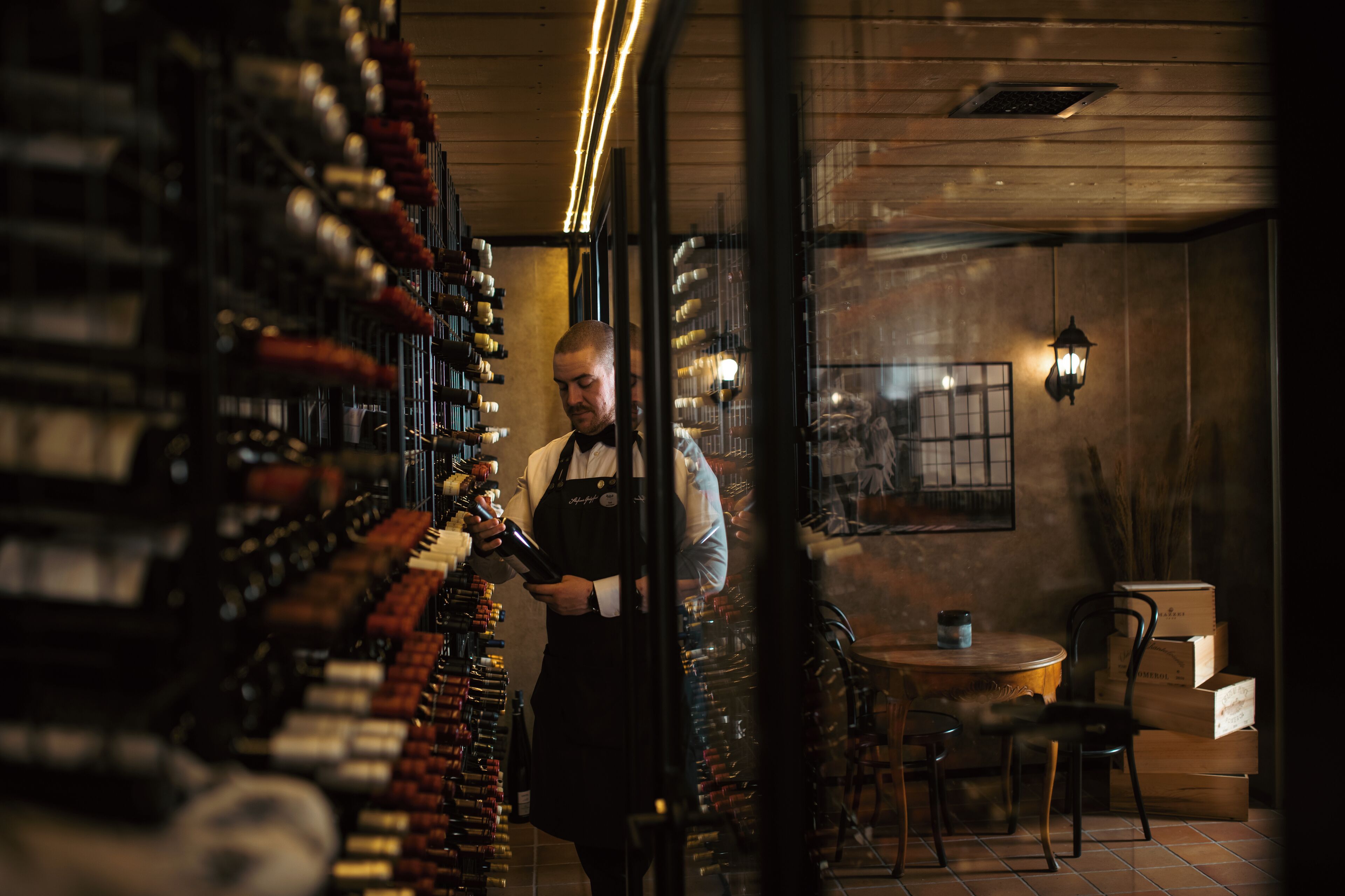 A bar with shelves of bottles, a bartender, and a table with chairs.