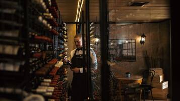 A bar with shelves of bottles, a bartender, and a table with chairs.