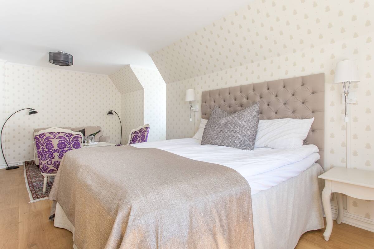 A hotel room with a large bed, a chair, a bedside table, and a lamp.