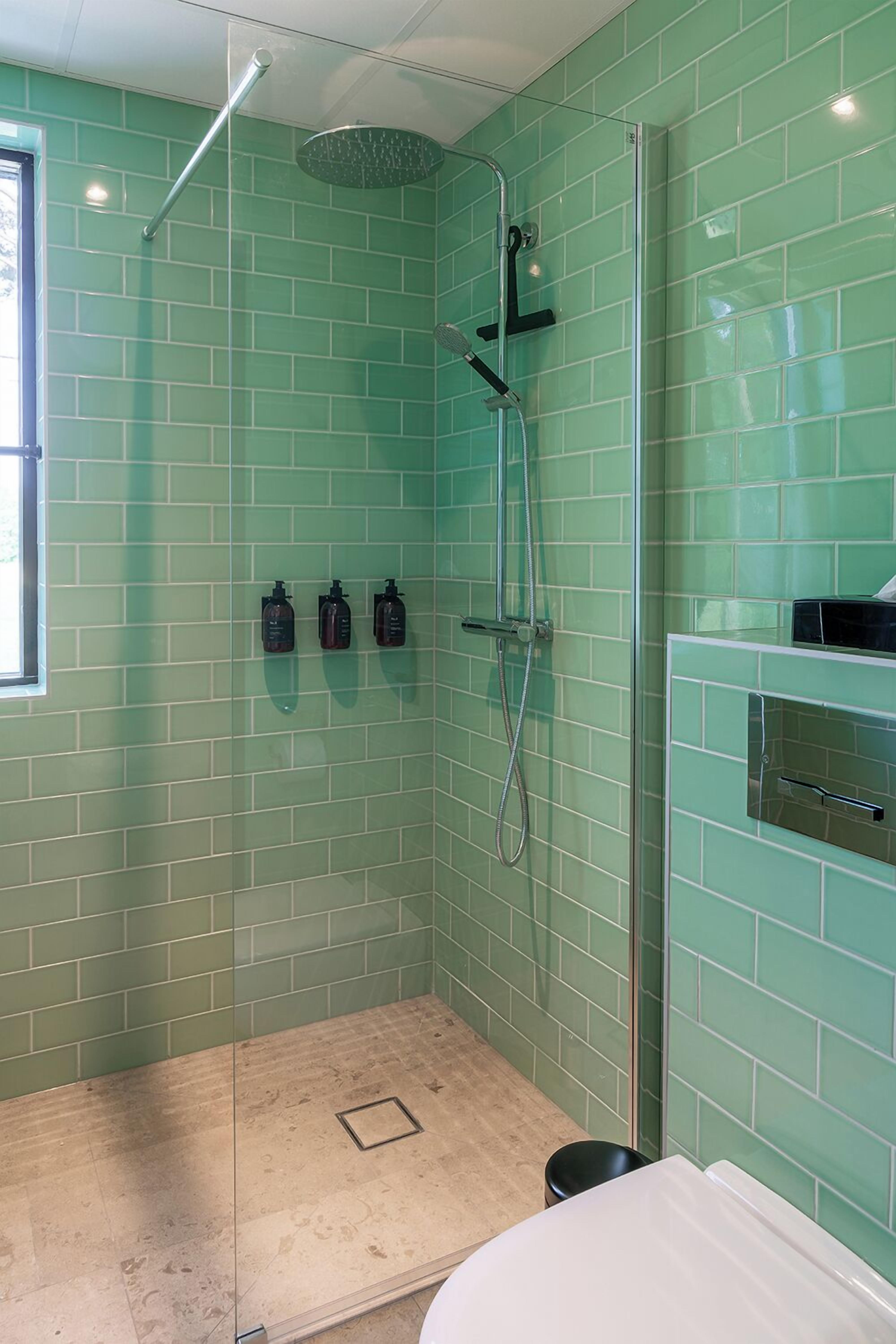 A modern bathroom with green tiled walls, a glass shower enclosure, and a white sink.