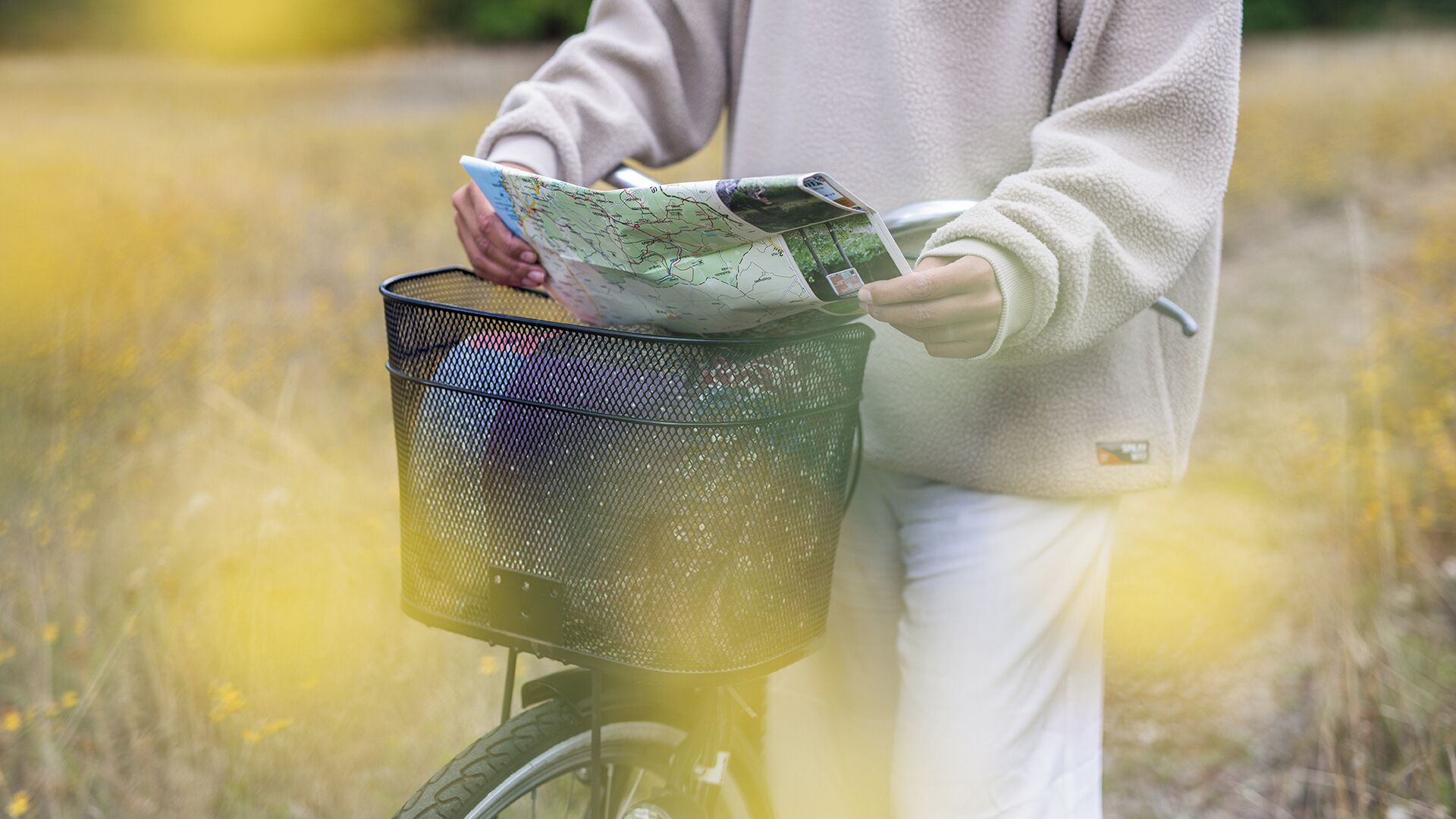 A person holding a map and a brochure, with a bicycle and a basket containing a map.