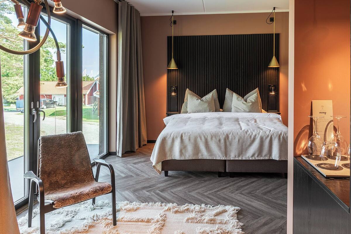 A modern bedroom with a large bed, a chair, a rug, and a view through the window.