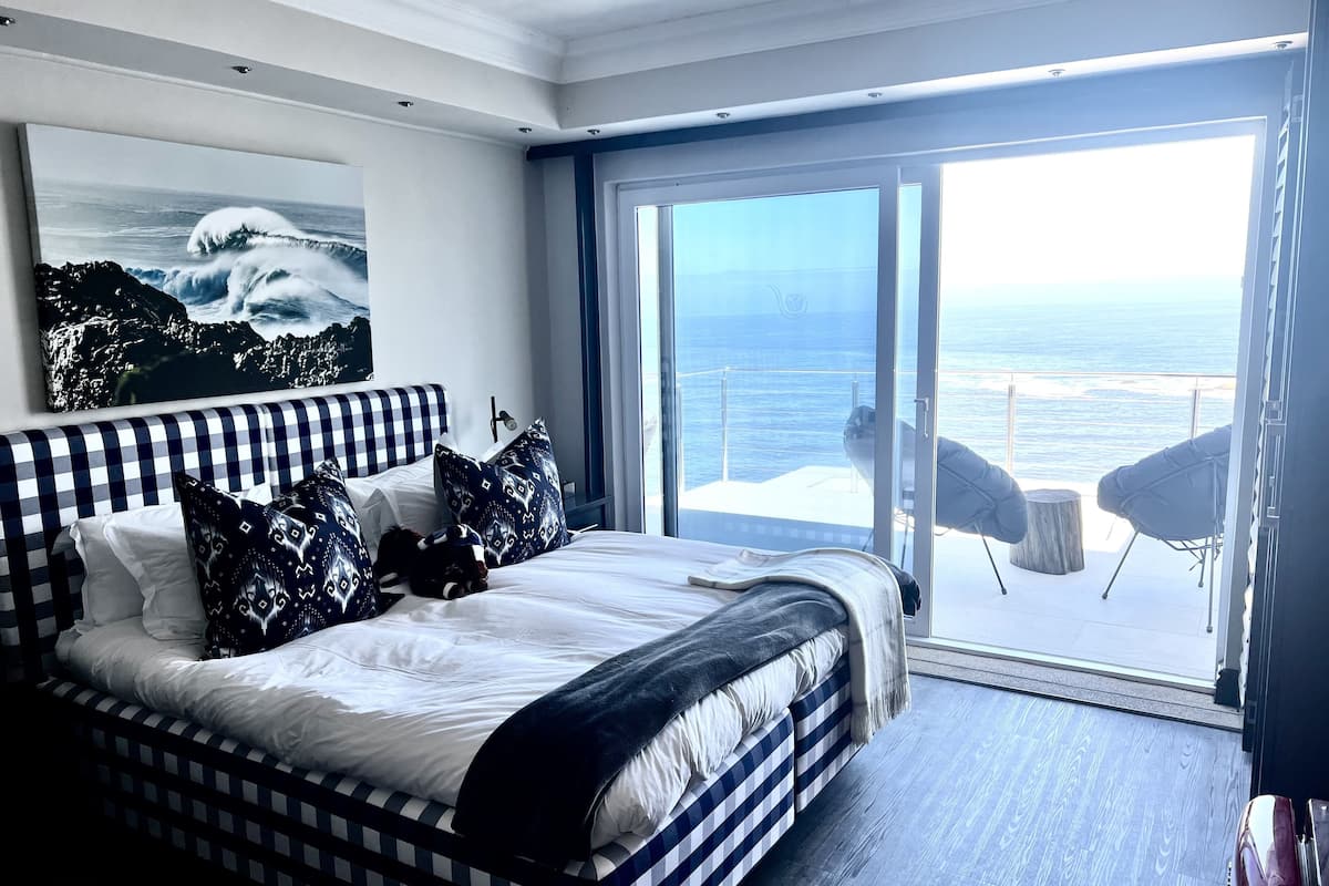 Un dormitorio con una cama grande, vistas al océano y un balcón con sillas.