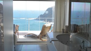 A modern bathroom with a large bathtub, a shower area, and a view of the ocean.