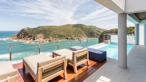 A deck with wooden flooring, a pool, and lounge chairs overlooking the ocean.