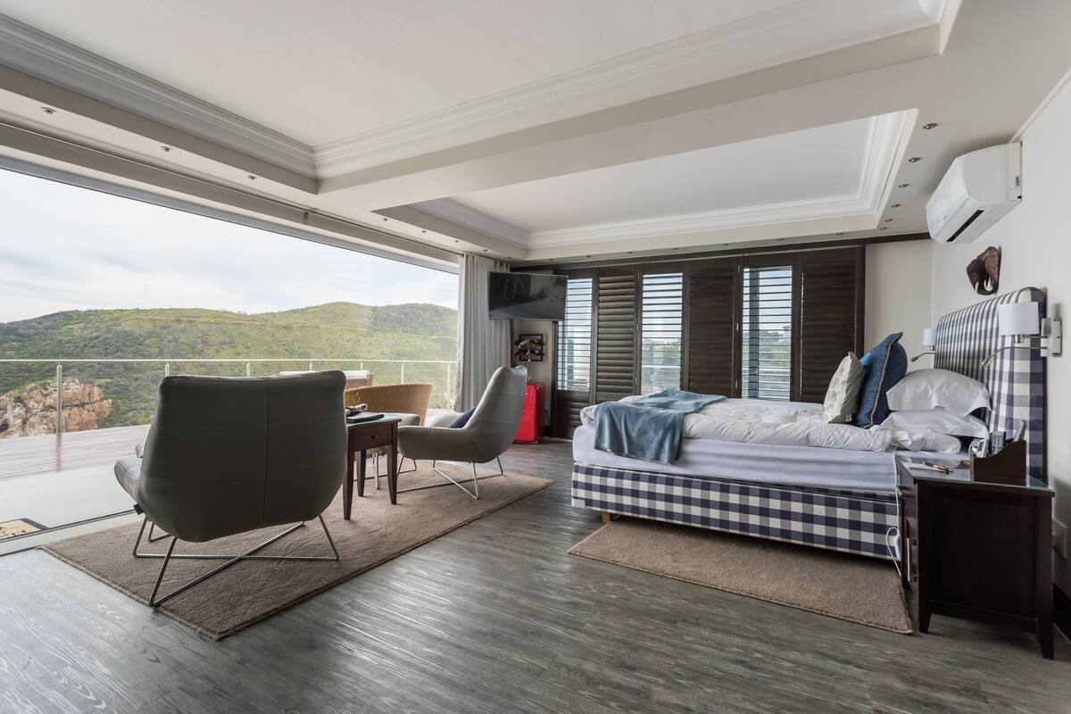 Un dormitorio moderno con un ventanal grande, una cama, una silla y un televisor.