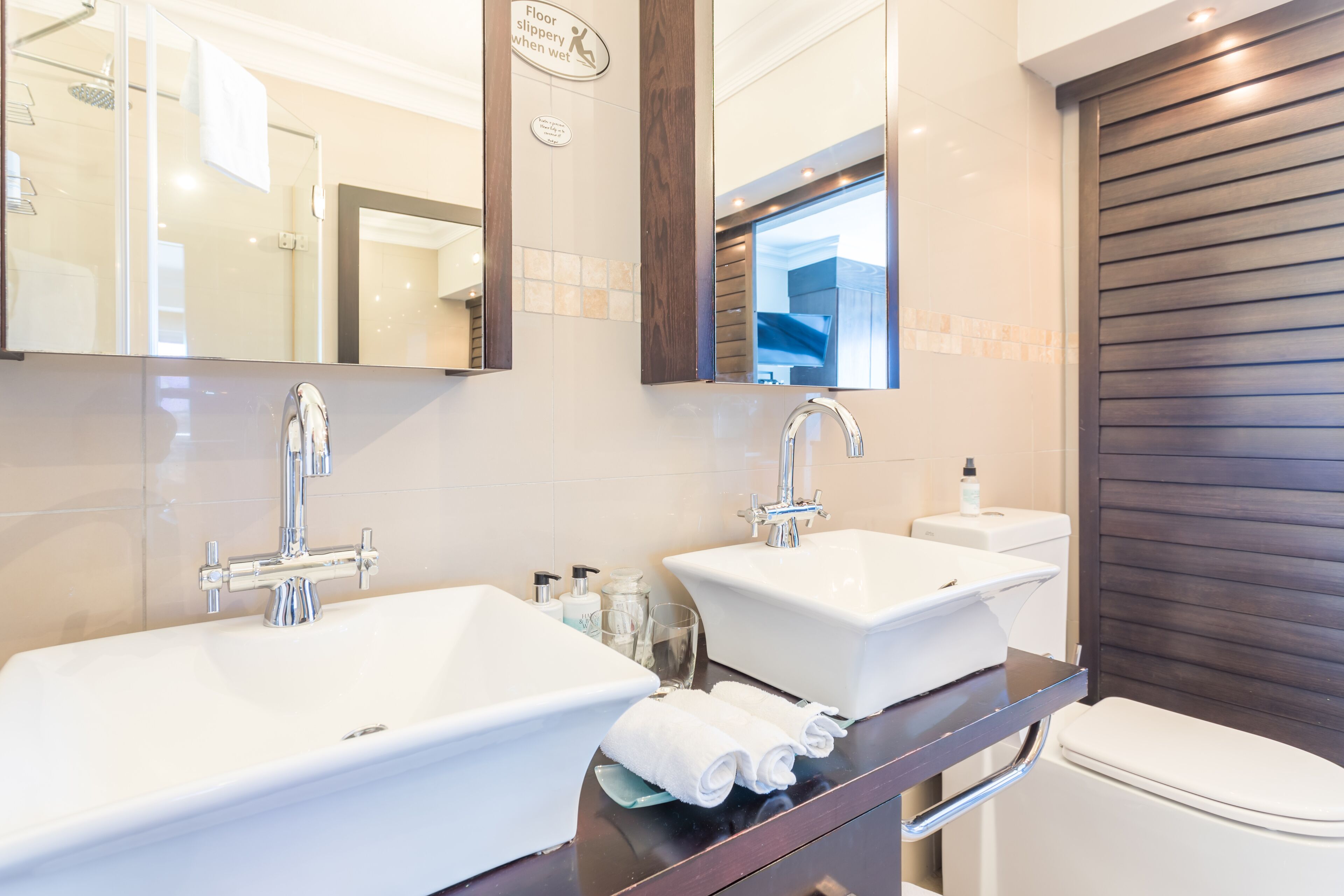 A modern bathroom with two sinks, a mirror, and a toilet.