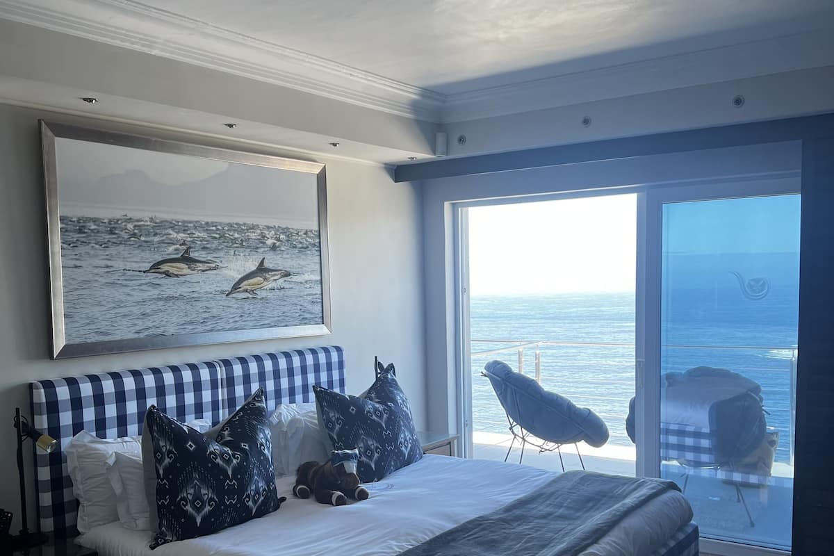 Un dormitorio con colcha a cuadros, un ventanal con vistas al mar y un cuadro colgado de ballenas.