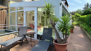 Un espacio de estar al aire libre techado con mesa y sillas, rodeado de plantas en macetas y una terraza de madera.