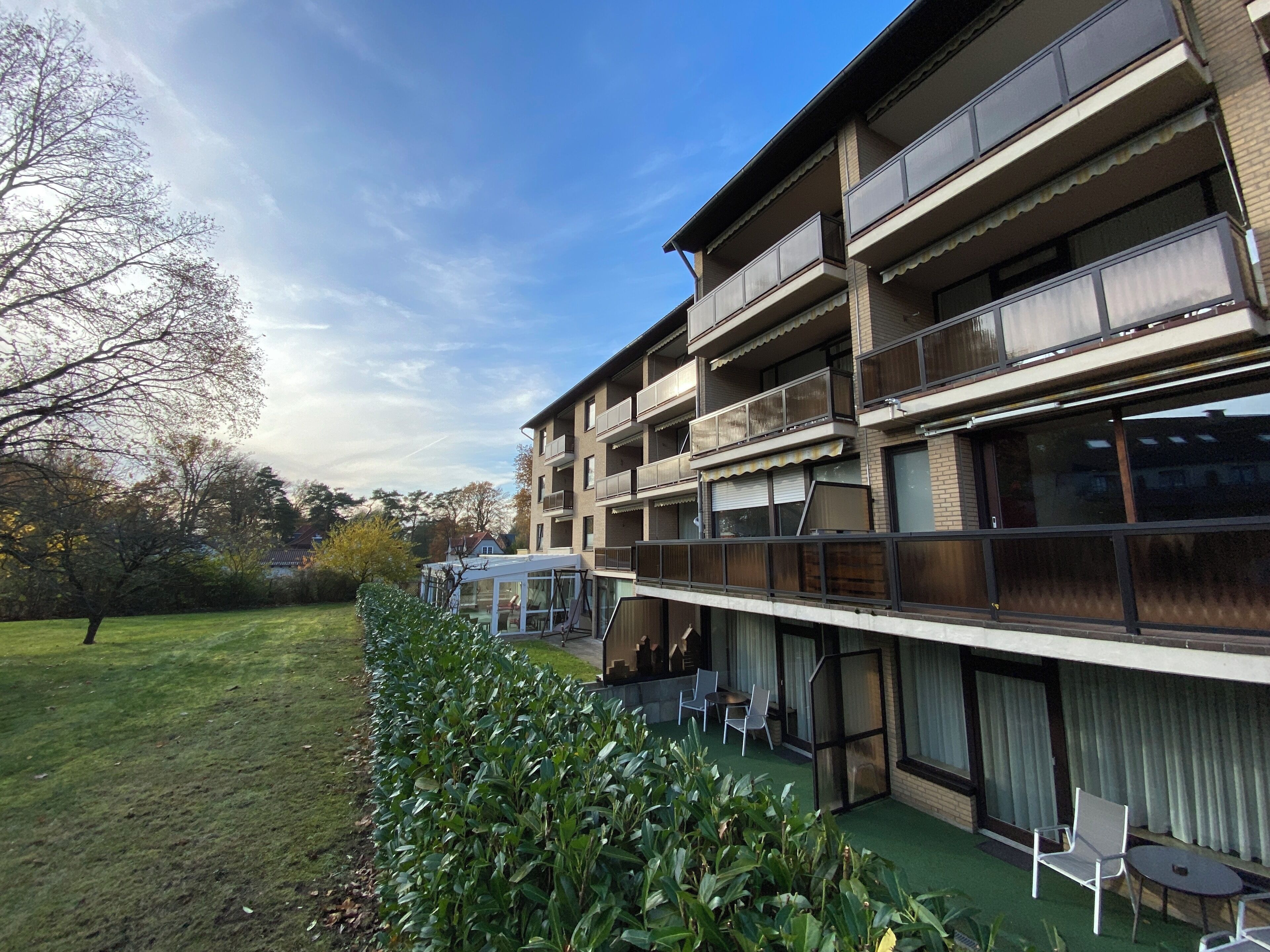 A multi-story building with balconies, a covered outdoor seating area, and a well-maintained lawn.