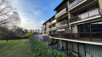 A multi-story building with balconies, a covered outdoor seating area, and a well-maintained lawn.