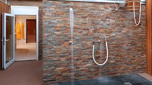 Un área de spa con pared de piedra, zona de ducha y puerta que da a un cuarto con toallas amarillas.