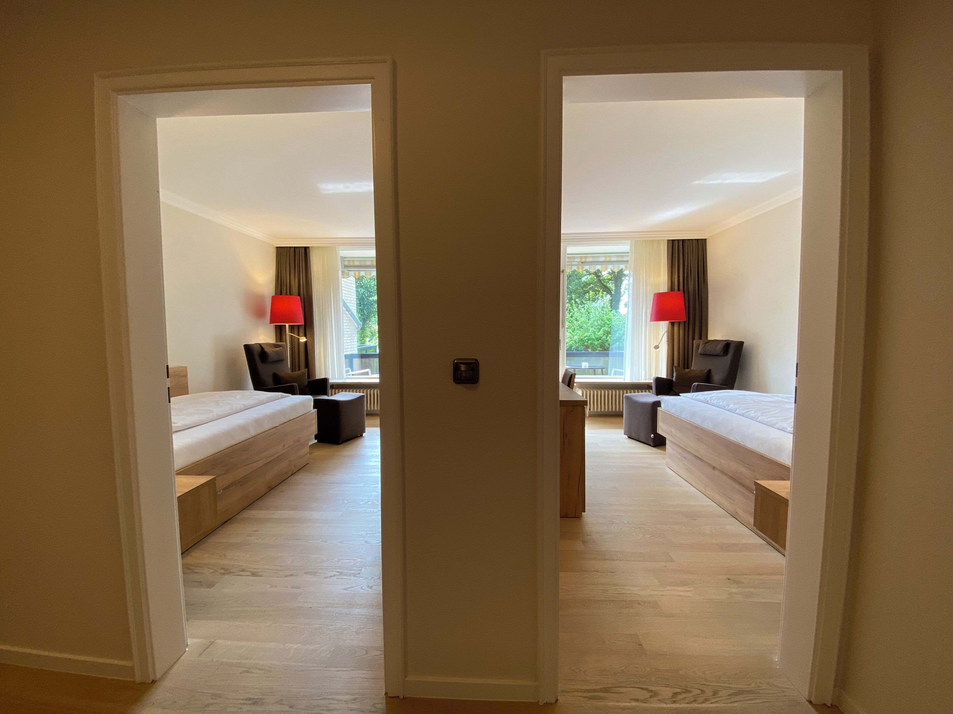 Een hotelkamer met twee bedden, een bureau en uitzicht op groen.