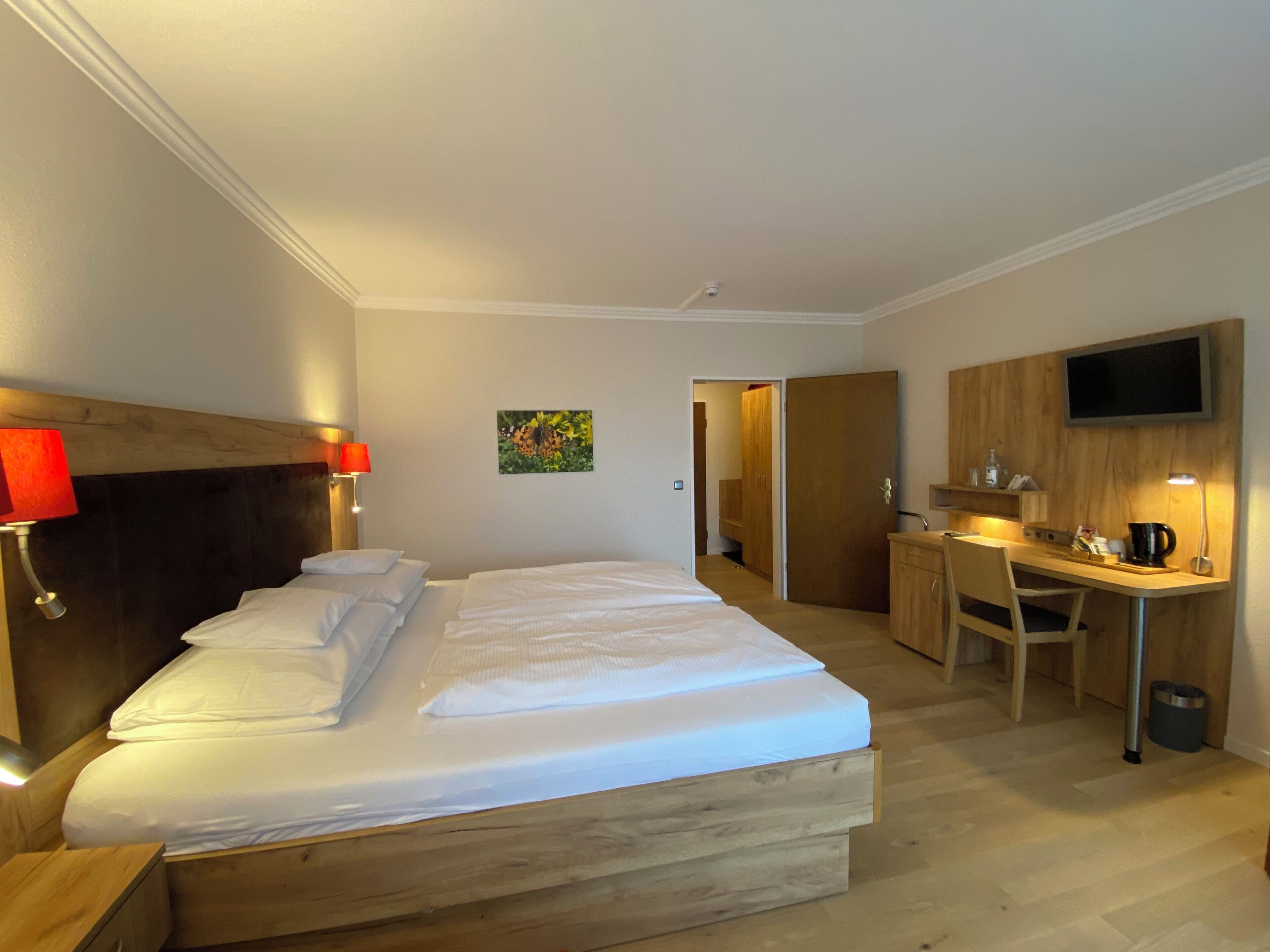 A hotel room with a wooden bed, a desk, and a TV on the wall.