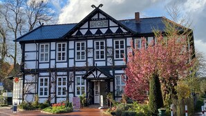 Un edificio tradicional con entramado de madera y una fachada simétrica, una entrada central y un jardín bien cuidado con plantas en flor.