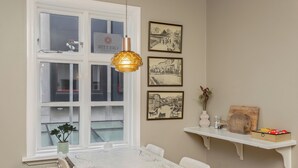 A dining area with a table, chairs, a hanging light fixture, a window, and wall-mounted shelves with items. - Grettir Guesthouse (Reykjavik)