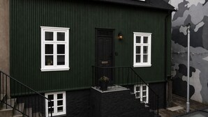 A green building with a black roof, white-framed windows, a black door, and a small porch with a black railing. - Grettir Guesthouse (Reykjavik)
