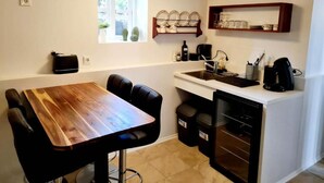 A compact kitchen with a wooden dining table, black chairs, a built-in oven, and a window with plants. - Grettir Guesthouse (Reykjavik)