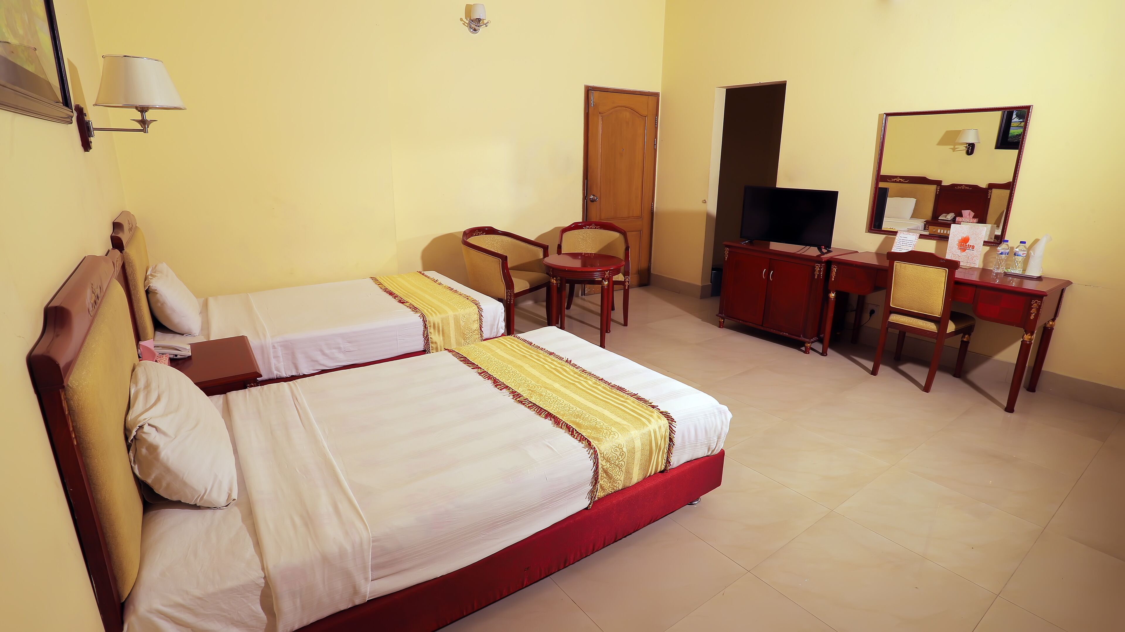 Quarto de hotel com duas camas, uma escrivaninha, uma cadeira, uma televisão e um guarda-roupa.