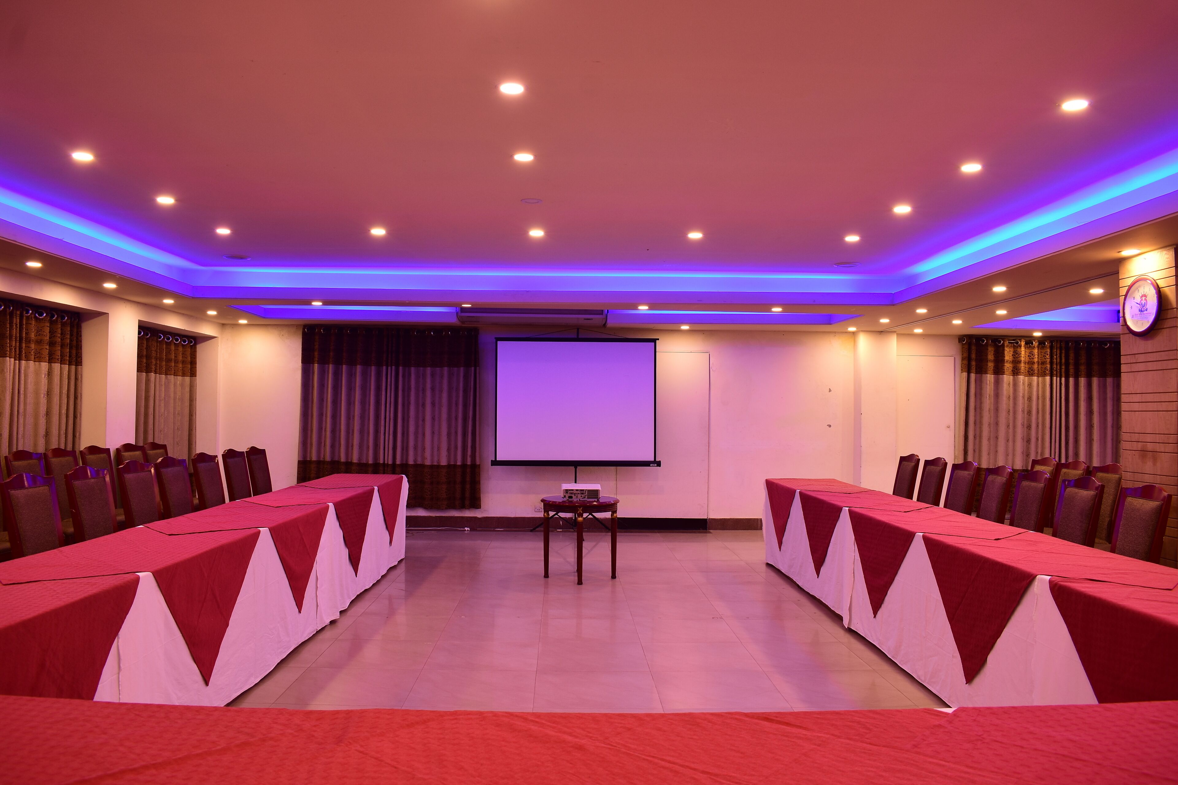 A conference room with a long table, chairs, a projector screen, and a stage.