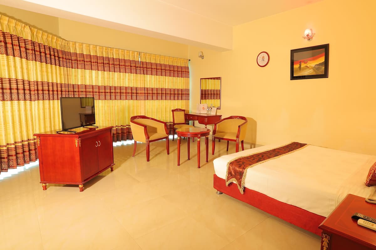 A hotel room with a bed, a desk, two chairs, a television, a clock, and a framed picture on the wall.