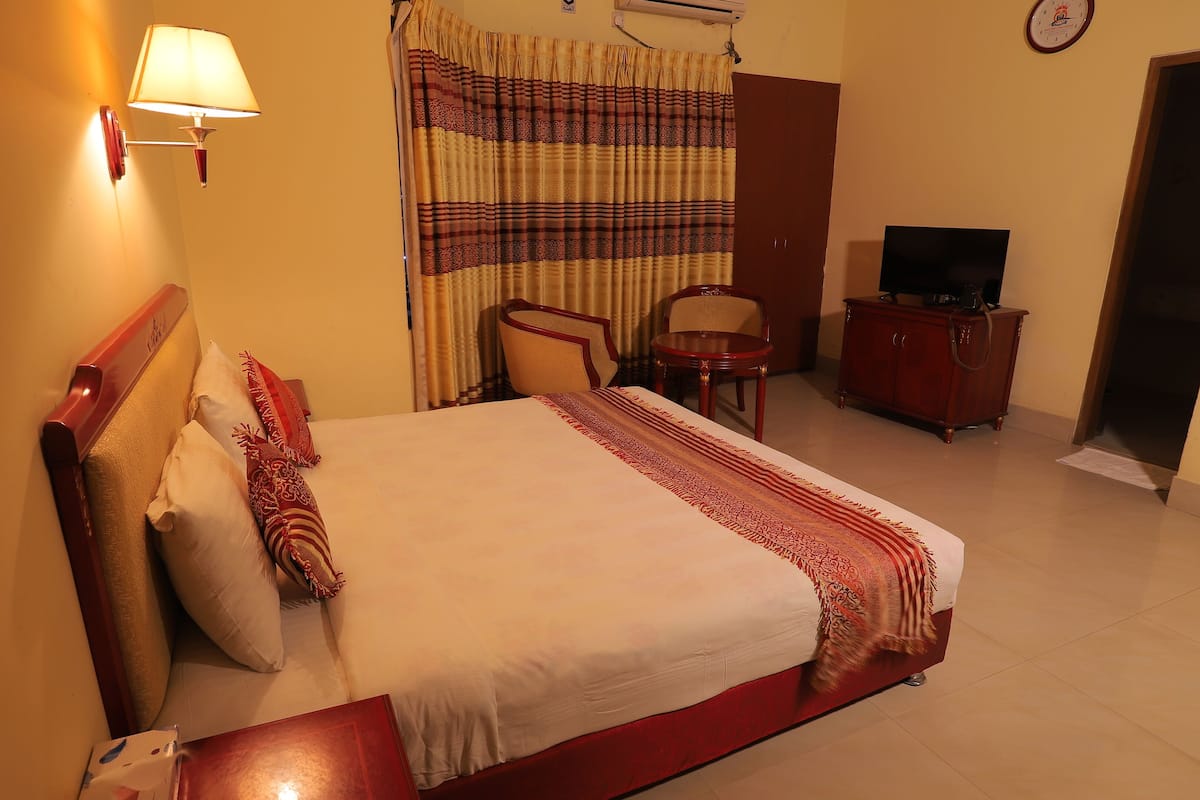 A hotel room with a bed, a chair, a small table, a television, and a wall-mounted air conditioner.