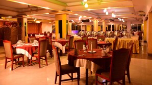 A restaurant with multiple tables and chairs, arranged in a spacious layout with a high ceiling and modern lighting fixtures. - Hotel Metro International (Sylhet)