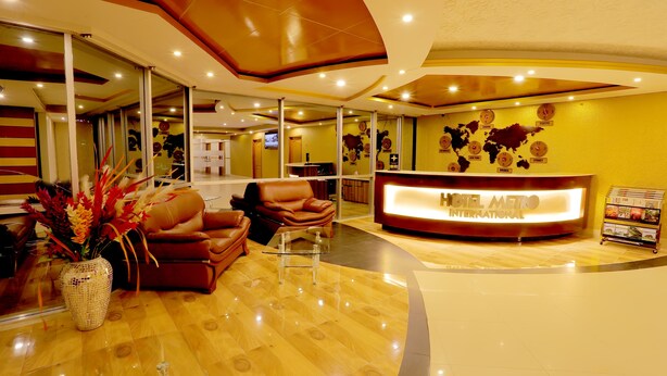 A hotel reception area with a modern design, featuring a reception desk, leather seating, and a decorative world map on the wall. - Hotel Metro International (Sylhet)
