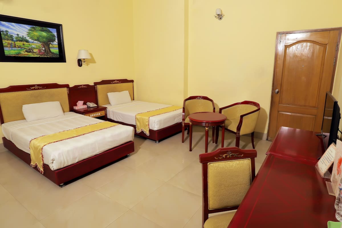 A hotel room with two beds, a small table, two chairs, a TV, and a door.