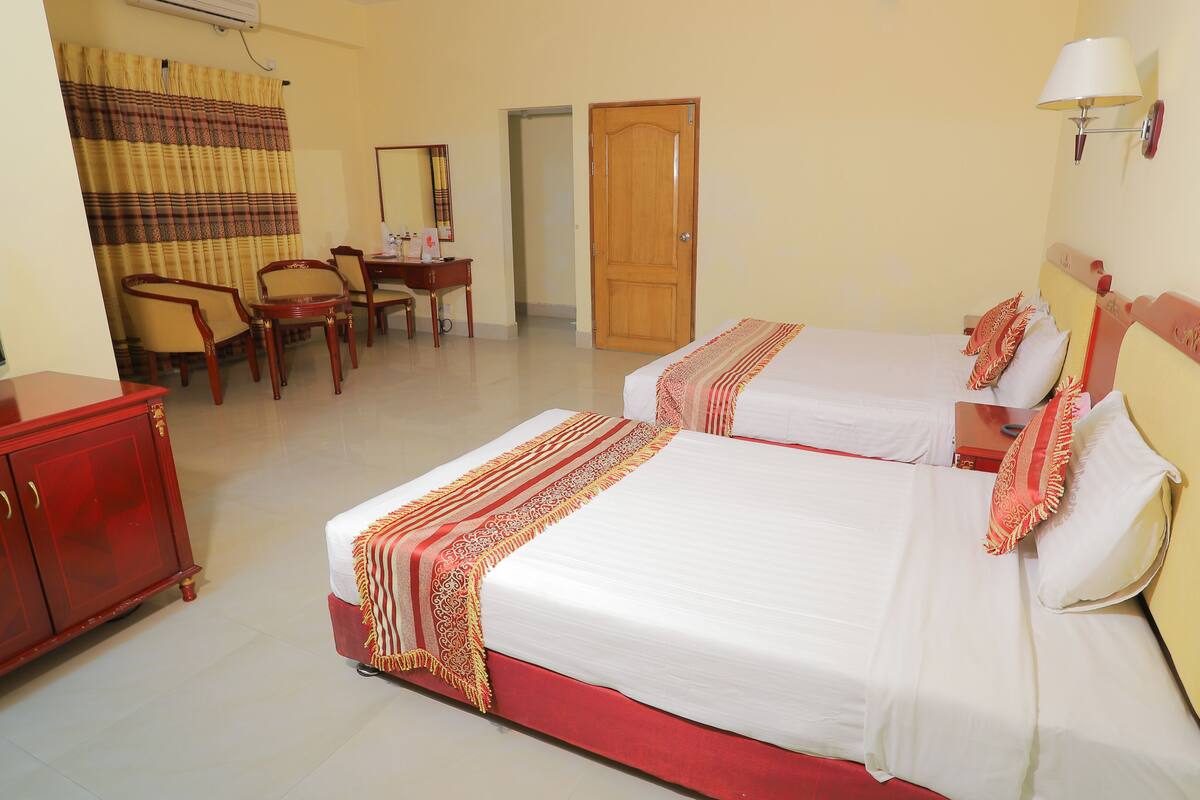 A hotel room with two beds, a television, a desk with a chair, and a wardrobe.