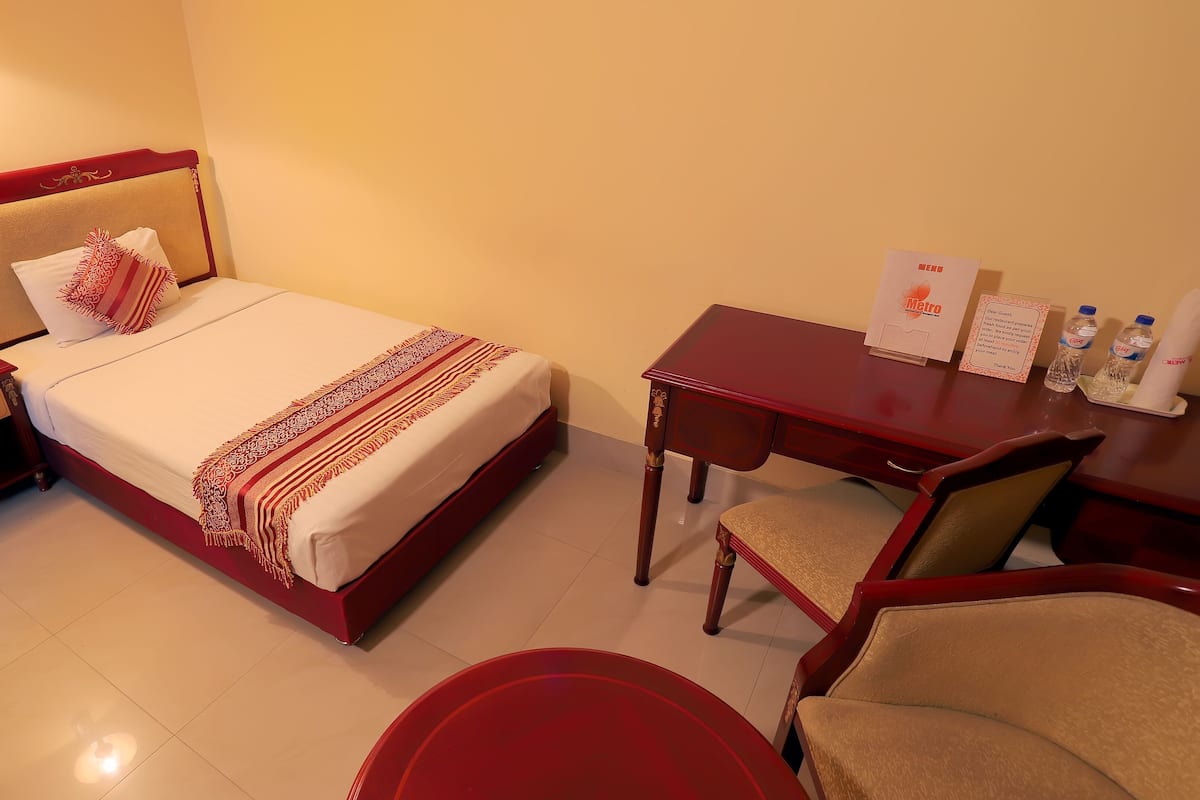 A hotel room with a bed, bedside table with a phone, a desk with a chair, and a table with water bottles.