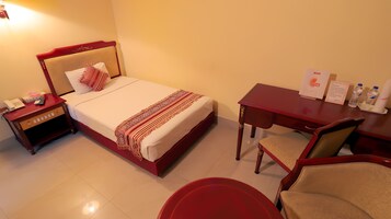 Habitación de hotel con cama, mesita de noche con teléfono, escritorio con silla y mesa con botellas de agua.