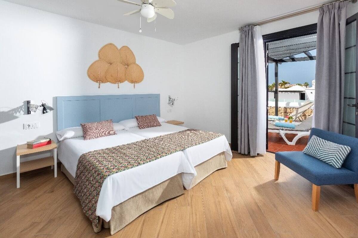 A hotel room with a bed, a chair, a ceiling fan, and a view of the outdoors.