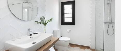 A modern bathroom with a large oval mirror, a white sink, a toilet, and a shower.