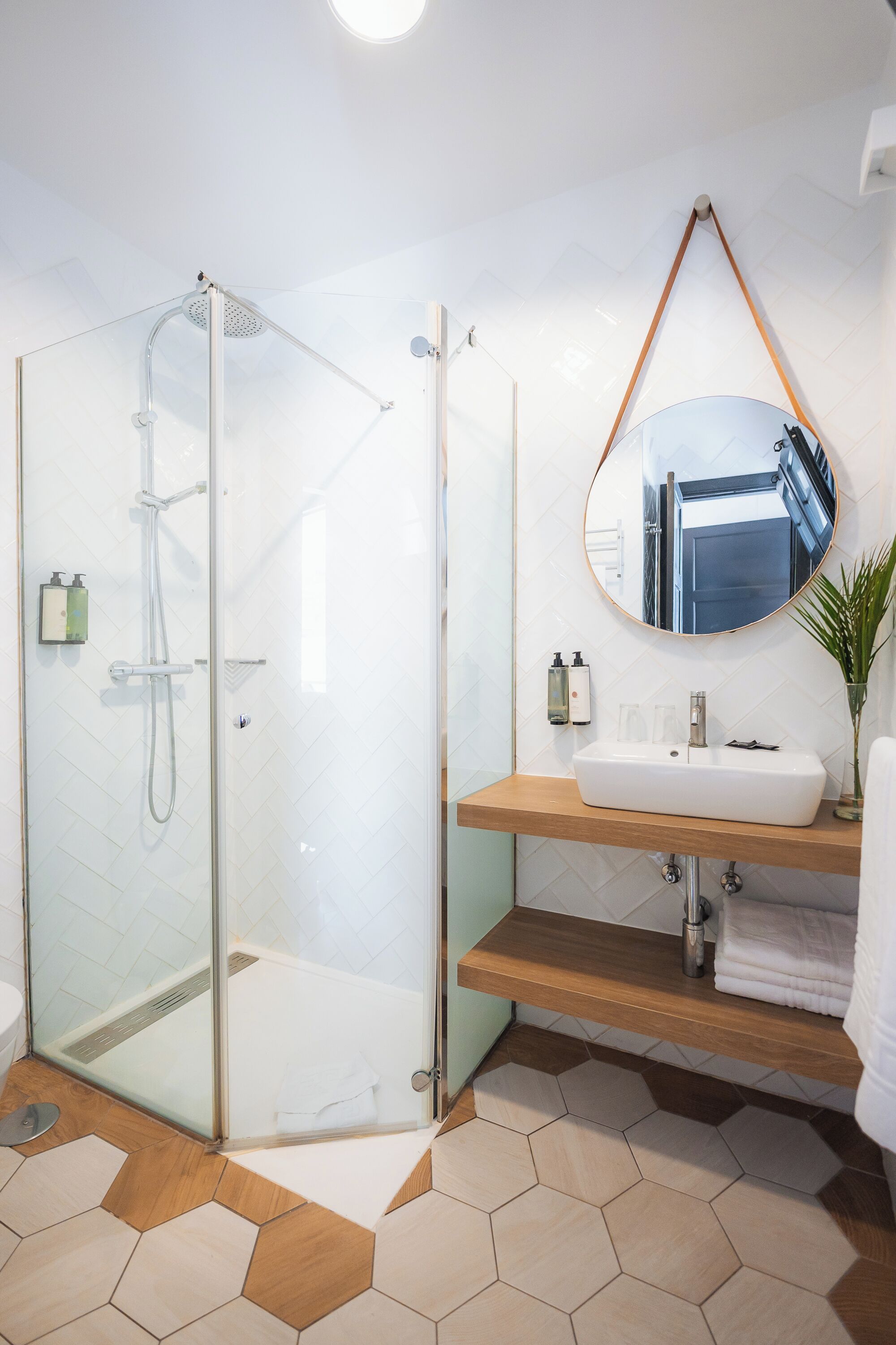 Een moderne badkamer met een douchecabine van glas, een houten wastafelmeubel met een wastafel en een spiegel erboven.