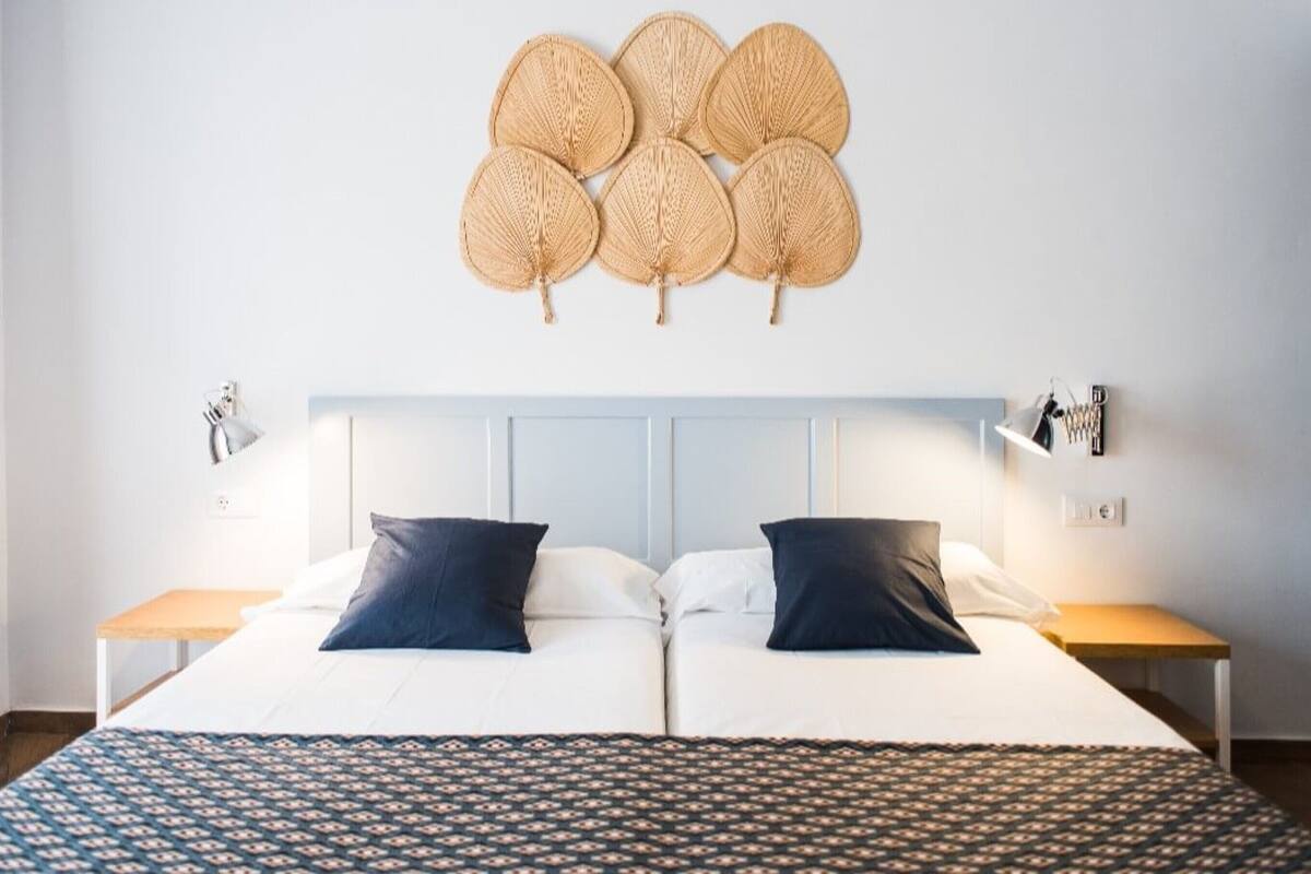 A hotel room with a large bed, two bedside tables, a wall-mounted lamp, and a decorative wall hanging.