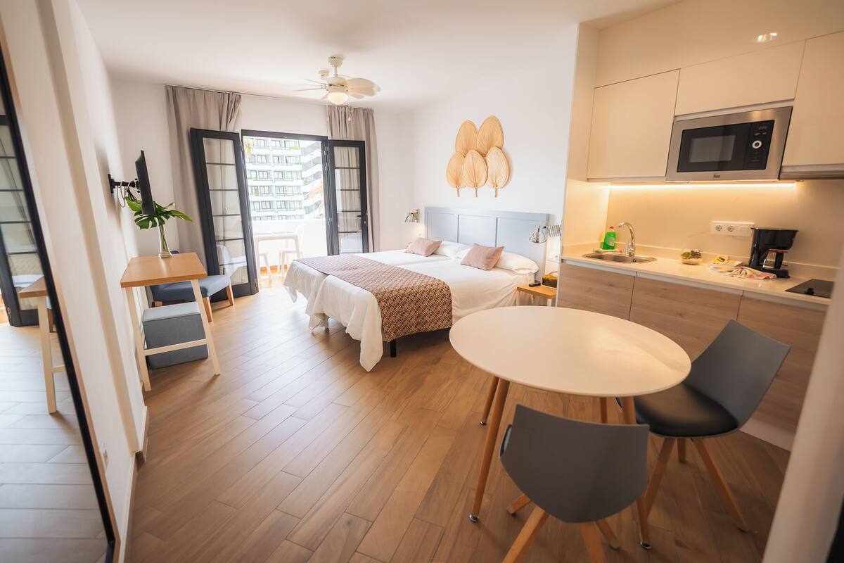 A modern hotel room with a bed, bedside table, and a small dining area with a table and chairs.