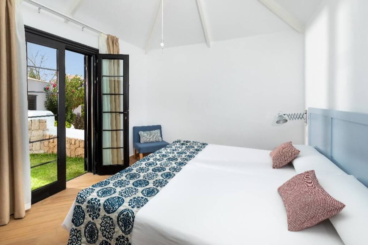 A bedroom with a bed, a chair, a window with curtains, and a view of the outside.