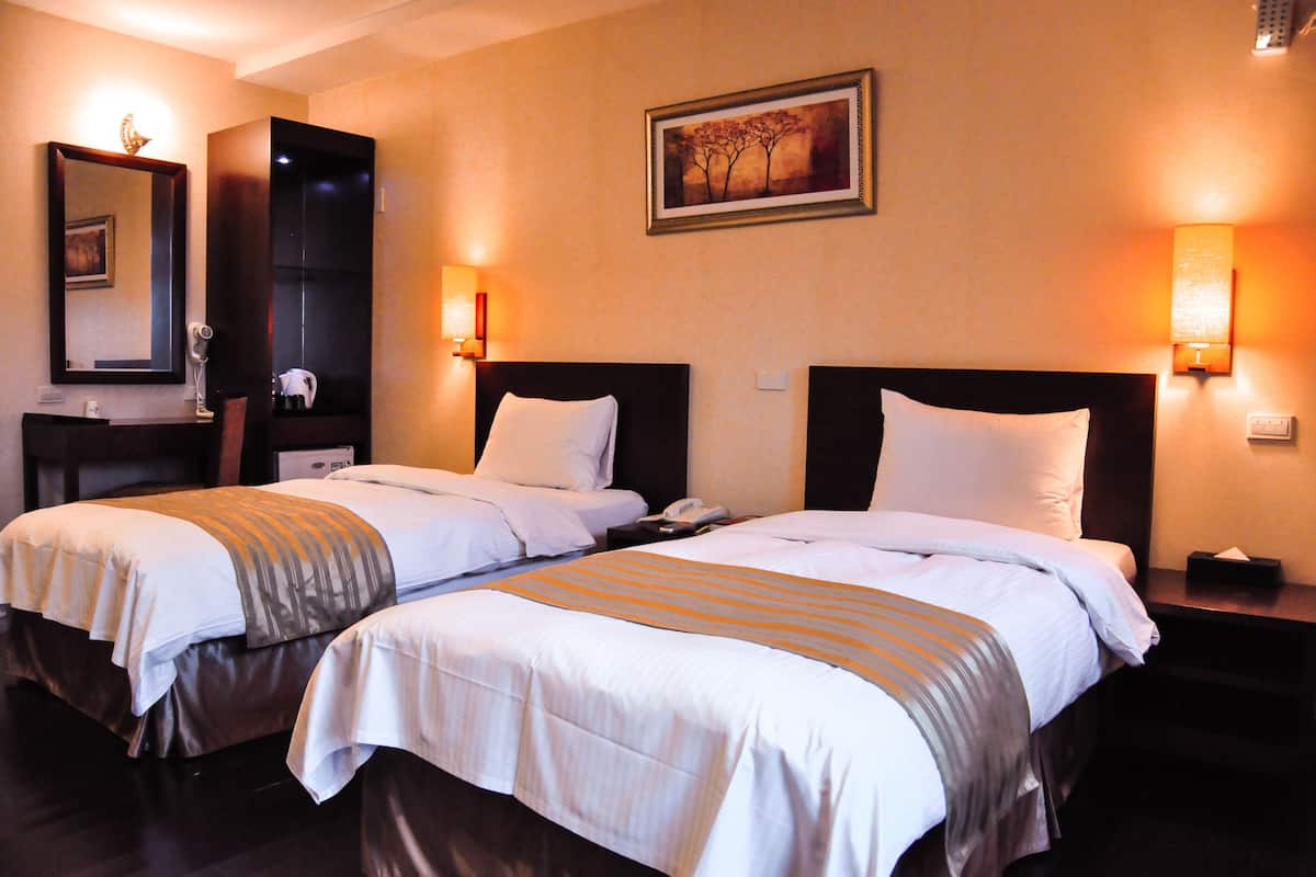 Een hotelkamer met twee bedden, een bureau, een spiegel en wandlampen.