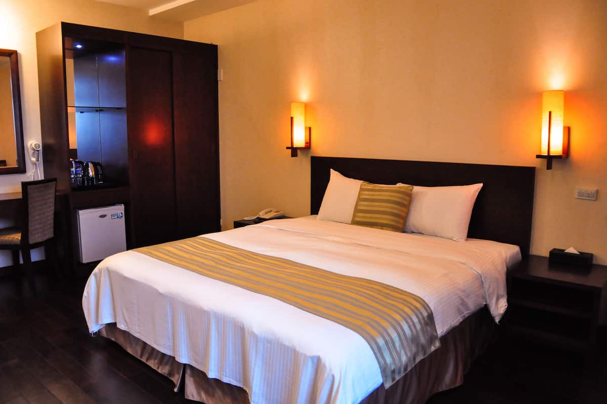 Een hotelkamer met een groot bed, twee bedlampen, een bureau met telefoon en een minibar.